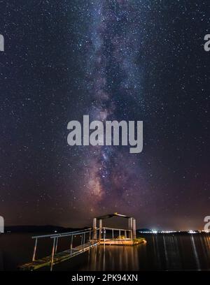 Via Lattea sul mare con un molo e una spiaggia di sabbia in primo piano. Stelle, colpo notturno, Ouranoupoli vicino a Salonicco, Grecia Foto Stock