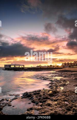Alba sulla spiaggia, rocce laviche e spiaggia sabbiosa in lunga esposizione. Posto romantico con molo al mattino. Playa de la Barreta, Parco Nazionale di Corralejo, Isole Canarie, Spagna Foto Stock