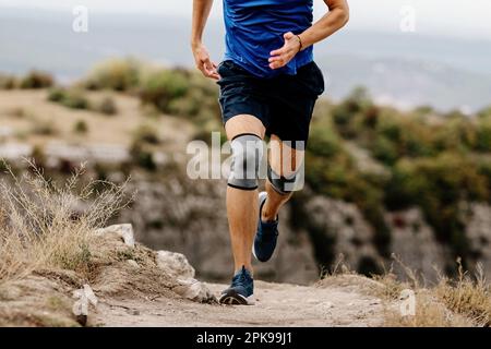 corridore maschio con ginocchiere che corrono su sentiero di montagna, maniche di compressione di protezione contro le lesioni per stabilizzare le gambe Foto Stock