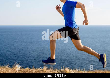 corridore maschio che corre sentiero di montagna sullo sfondo del mare e del cielo, jogging estivo lungo la costa Foto Stock