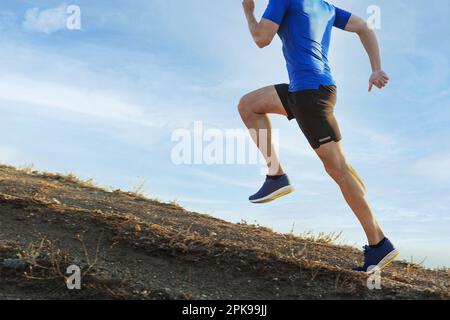 maschio runner correre ripida salita di montagna su sentiero in cielo blu sfondo, superando le difficoltà sportive Foto Stock