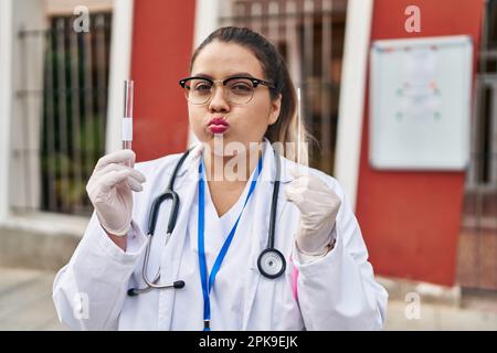 Giovane donna medico ispanica che fa l'infezione da coronavirus test nasale puffing guance con faccia divertente. bocca gonfiata con aria, che cattura l'aria. Foto Stock