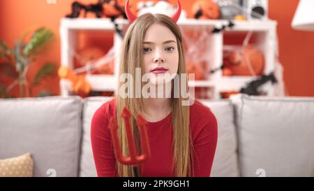 Giovane donna bionda che indossa il costume diavolo seduto sul divano a casa Foto Stock