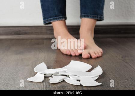 Donna a piedi nudi in piedi vicino al piatto rotto sul pavimento, primo piano Foto Stock