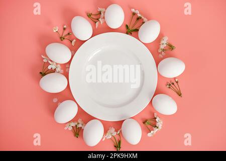 Composizione con piatto vuoto, uova di Pasqua e bellissimi fiori su sfondo rosa, primo piano. Spazio per la copia. Vista dall'alto. Foto Stock