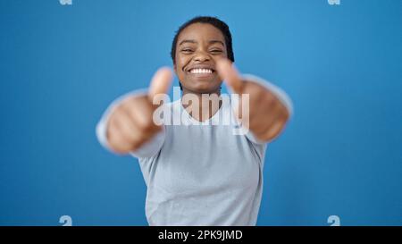Donna afroamericana sorridente con i pollici su sopra lo sfondo blu isolato Foto Stock