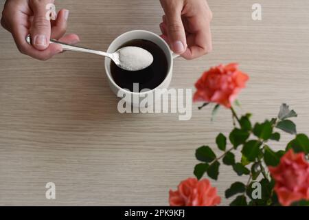 Donna che aggiunge zucchero al caffè del mattino al tavolo di legno, vista dall'alto Foto Stock