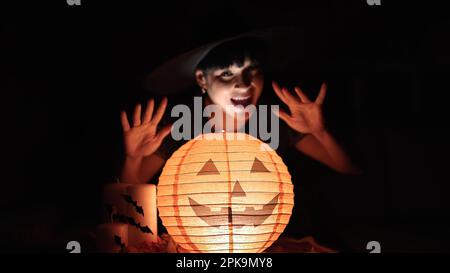 Giovane donna cinese che indossa costume da strega con lampada di zucca di Halloween a casa Foto Stock