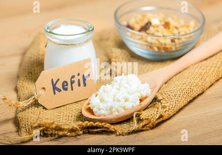 Grani di kefir in cucchiaio di legno davanti a tazze di yogurt di kefir parfaits. Kefir è uno dei migliori alimenti per la salute disponibili fornendo probiotici potenti. Foto Stock
