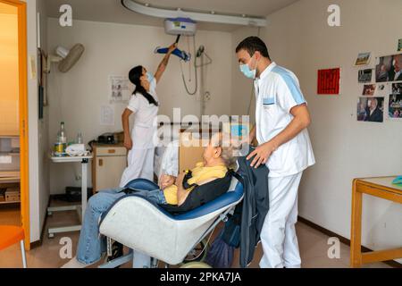 Due assistenti infermieri mettono un paziente disabili a letto nella sua stanza presso la casa di cura. Foto Stock