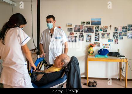 Due assistenti infermieri mettono un paziente disabili a letto nella sua stanza presso la casa di cura. Foto Stock