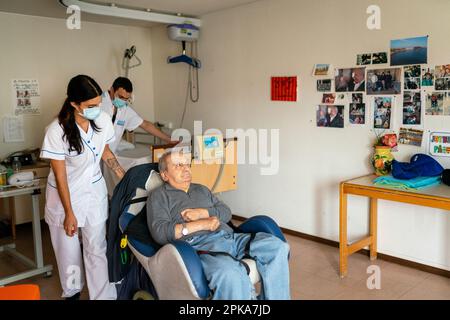 Due assistenti infermieri mettono un paziente disabili a letto nella sua stanza presso la casa di cura. Foto Stock