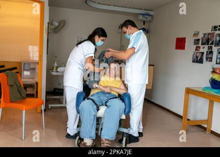 Due assistenti infermieri mettono un paziente disabili a letto nella sua stanza presso la casa di cura. Foto Stock