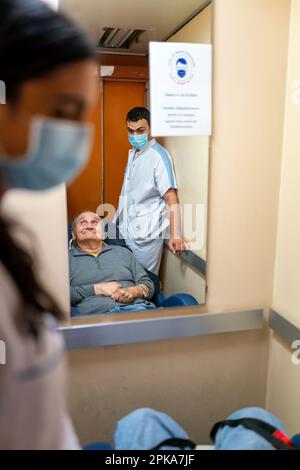 Due assistenti infermieri mettono un paziente disabili a letto nella sua stanza presso la casa di cura. Foto Stock