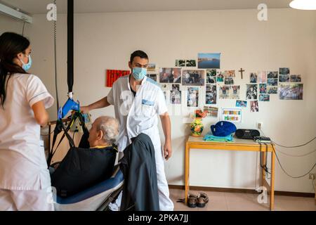 Due assistenti infermieri mettono un paziente disabili a letto nella sua stanza presso la casa di cura. Foto Stock