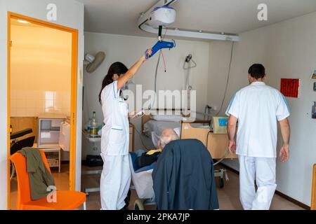 Due assistenti infermieri mettono un paziente disabili a letto nella sua stanza presso la casa di cura. Foto Stock