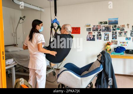 L'operatore sanitario prepara l'ora di andare a letto di un paziente disabile nella sua stanza presso la casa di riposo. Foto Stock