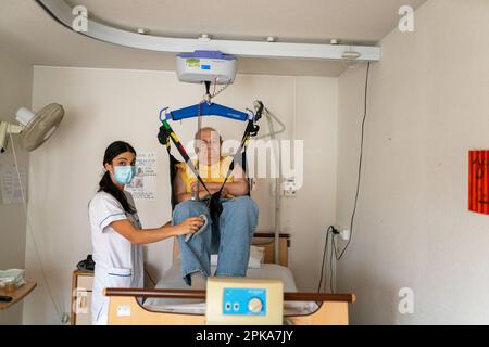 L'operatore sanitario prepara l'ora di andare a letto di un paziente disabile nella sua stanza presso la casa di riposo. Foto Stock