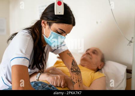 L'operatore sanitario prepara l'ora di andare a letto di un paziente disabile nella sua stanza presso la casa di riposo. Foto Stock