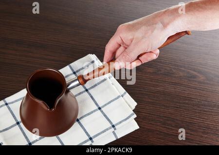 Mano da uomo che tiene il turk del caffè. Cezve di argilla per preparare il caffè in mano Foto Stock