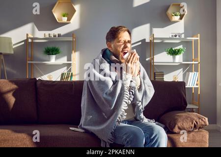 Giovane malato avvolto in coperta starnuti e tosse Foto Stock