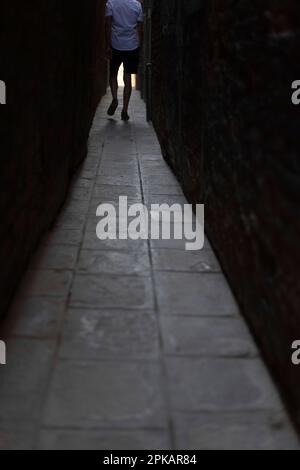 Uomo che cammina attraverso un vicolo stretto e cupo a Venezia Foto Stock