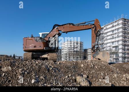 L'escavatore marrone si trova in un grande cantiere con edifici a conchiglia a più piani sullo sfondo Foto Stock