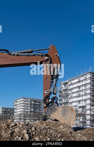 Pala di escavatore marrone si trova in un grande cantiere con edifici a conchiglia a più piani sullo sfondo Foto Stock