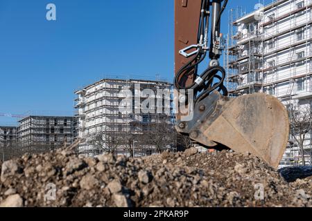 Pala di escavatore marrone si trova in un grande cantiere con edifici a conchiglia a più piani sullo sfondo Foto Stock