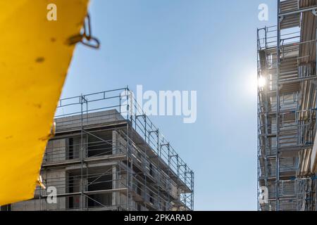 Contenitore giallo per rifiuti di costruzione stand di fronte a ponteggi con cielo blu Foto Stock