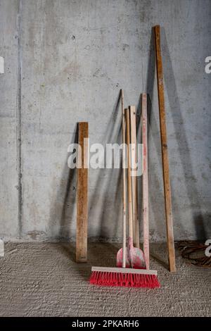 Scopa a pala e trave in legno appoggiata contro la parete in cemento in cantiere Foto Stock