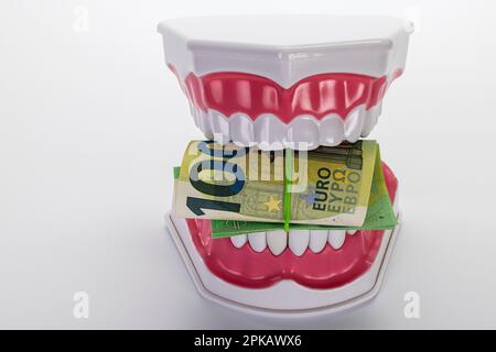 Modello di cura dentale aperto, 100 banconote in euro arrotolate insieme con fascia in gomma, immagine simbolo, protesi dentarie, corpagamento, spese dentarie, sfondo bianco, Foto Stock