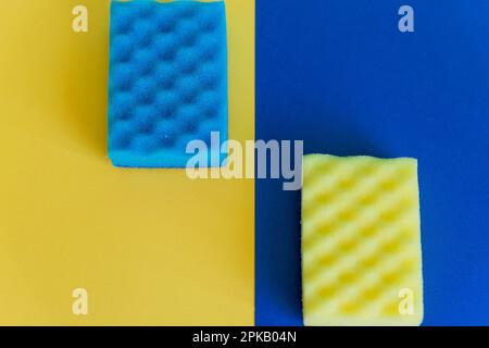 Spugne per lavastoviglie gialle e blu su sfondo colorato. Composizione vista dall'alto con spazio di copia. Concetto di pulizia. Colori nazionali dell'Ucraina. Foto Stock