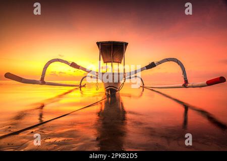 Tradizionale barca da pesca Jukung in un tramonto da sogno sulla spiaggia e il mare di Sanur, Denpasar, Bali, Indonesia Foto Stock