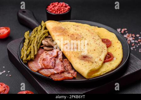 Deliziosa omelette fresca con pomodori ciliegini, pancetta, asparagi e spezie su fondo di cemento scuro Foto Stock