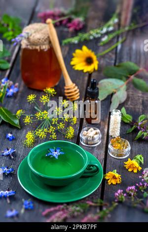 Tisane, integratori alimentari, omeopatia, miele, olio essenziale circondato da piante medicinali e fiori. Foto Stock