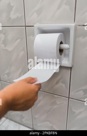 immagine della mano di una donna che srotola una carta igienica Foto Stock