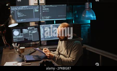Ingegnere di sistema informatico che confronta i file di dati su appunti cartacei e più monitor per programmare una nuova interfaccia server. Sviluppo di script html su una finestra terminale, codifica database. Scatto manuale. Foto Stock