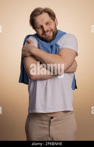 Vieni da me, voglio abbracciarti. Il bell'uomo caucasico si distese le mani e ti abbraccia. Espressione piacevole, sentimenti d'amore. Giovane ragazzo isolato da solo su sfondo beige studio. Stili di vita delle persone Foto Stock