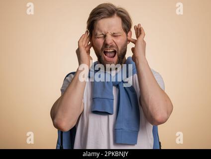 Non vuoi ascoltare e ascoltare. Frustrato annoiato irritato caucasico uomo che copre le orecchie gesturing No, evitando consiglio ignorando sgradevole rumore voci forte. Bel ragazzo solo su sfondo beige Foto Stock