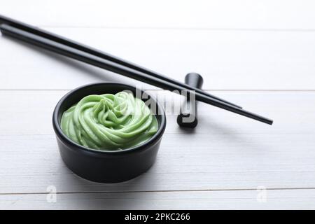 Ciotola con un vortice di pasta wasabi e bacchette su un tavolo di legno bianco Foto Stock