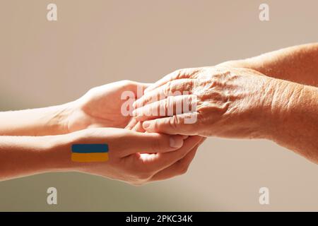 Aiuto per l'Ucraina. Persone che tengono le mani con disegno di bandiera Ucraina su sfondo chiaro, primo piano Foto Stock