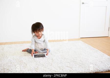 Bambino che guarda il tablet su un tappeto bianco Foto Stock