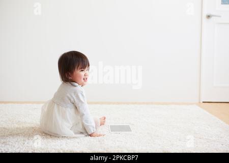 Il bambino si gira e ride con un tablet sul tappeto bianco Foto Stock