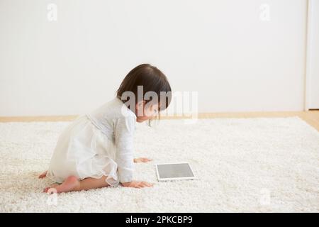 Bambino che guarda il tablet su un tappeto bianco Foto Stock