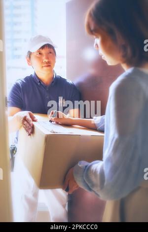 Uomo in abiti da lavoro che consegna scatole di cartone all'ingresso e donna che riceve le scatole Foto Stock