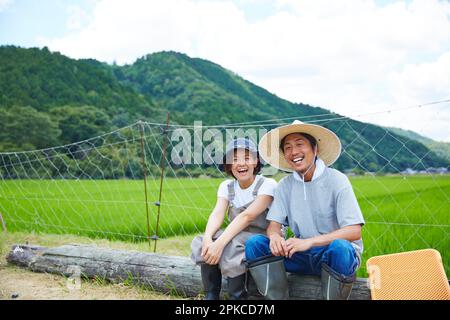 Sorridenti uomini e donne seduti su un log di fronte a un risone campo Foto Stock