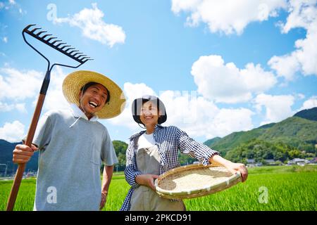 Uomini e donne che detengono attrezzi agricoli di fronte a un risaie Foto Stock