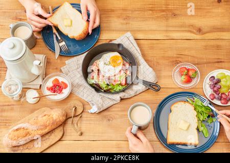 Pane, frutta, ecc. allineati su un tavolo di legno con due mani da donna Foto Stock