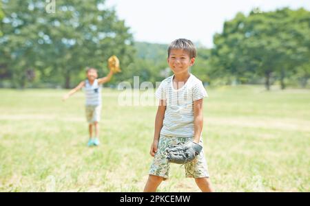 Fratelli che giocano a baseball sull'erba del parco Foto Stock